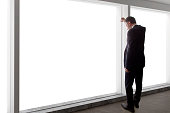 Middle aged businessman looking out a bright office window and thinking.  The entrepreneur is middle aged and wearing a suit.  He looks like he is a boss or CEO.  He is in an office loft with big windows.