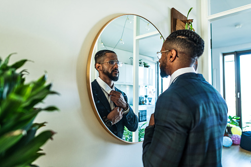 Young man at his home ties the tie in front of the mirror