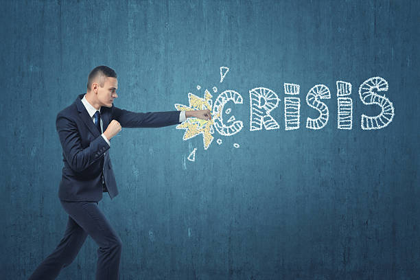 Businessman punching hard the word 'crisis' written on dark blue stock photo