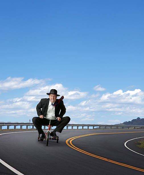 Businessman Racing On A Tricycle A businessman gritting his teeth while riding a tricycle on the open highway. There is room for text. adult tricycle stock pictures, royalty-free photos & images