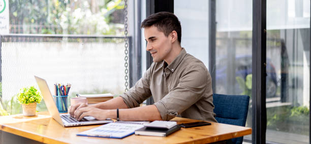 A businessman sits in his office with a laptop and stationery, on his desk there are financial documents he is checking, he is typing, texting, talking to his partner through a laptop messenger. stock photo