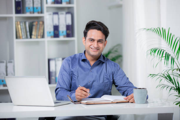 Businessman sitting at his desk and using laptop in the office stock photo Indian, office, businessman, employee, laptop, young man, employees at office stock pictures, royalty-free photos & images