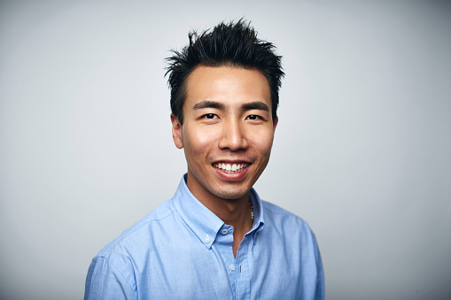 Portrait of smiling young businessman. Happy executive is wearing blue shirt. He is against white background.