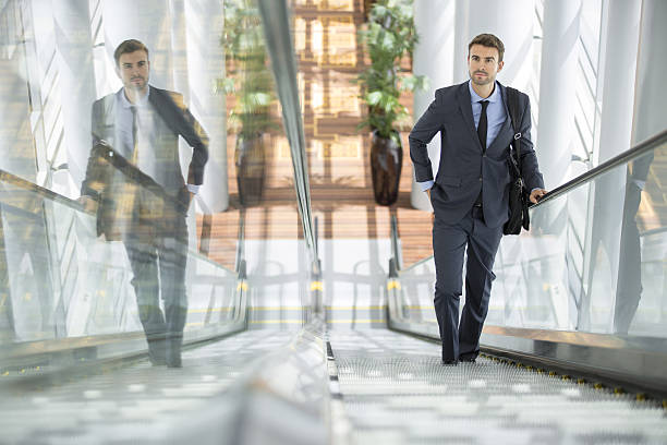 Businessman smiling with his own reflection at the escalator stock photo