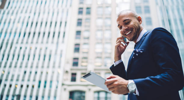 Businessman talking on cellphone and happily laughing while reading from tablet stock photo