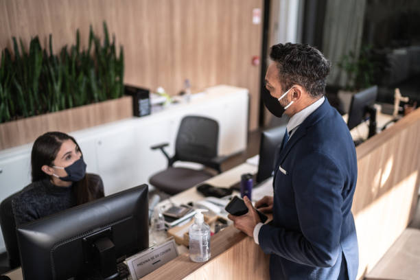 Businessman talking to receptionist on entrance of office's lobby - with face mask Businessman talking to receptionist on entrance of office's lobby - with face mask hotel reception photos stock pictures, royalty-free photos & images