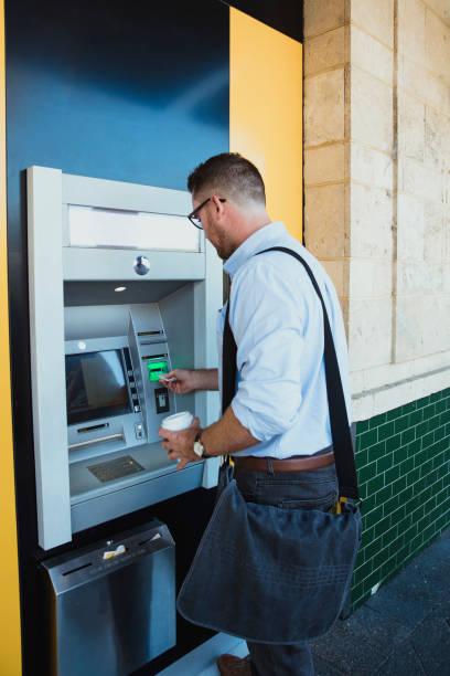 Businessman Using ATM Machine A rear-view shot of a caucasian businessman using an ATM machine in Perth Australia, he is inserting his credit card to withdraw money. banks and atms stock pictures, royalty-free photos & images