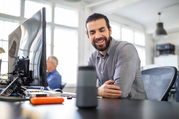 Businessman using digital speaker at office Businessman sitting at his desk talking to smart speaker. Male professional asking digital assistant a question at office. speech recognition stock pictures, royalty-free photos & images
