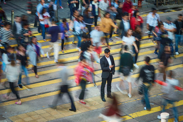 Businessman using smart phone amidst crowd High angle view of businessman using smart phone amidst crowd. Professional is standing on busy street. He is surrounded by people in city. hong kong photos stock pictures, royalty-free photos & images