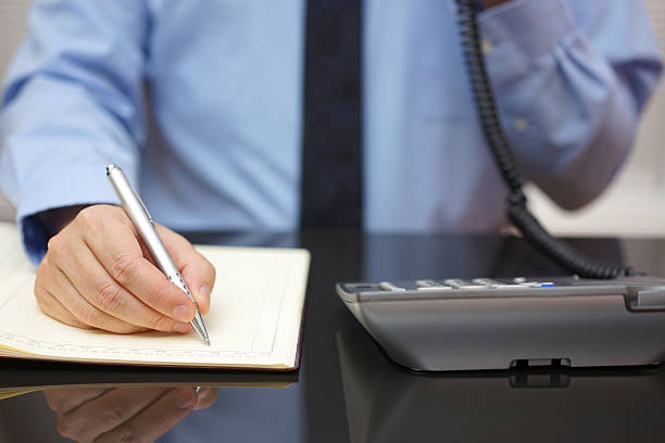 businessman-using-telephone-while-writing-in-notebook-at-desk