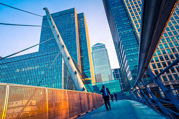 Businessman walking on a contemporary bridge in Canary Wharf, London Businessman walking on a contemporary bridge in Canary Wharf, London. Fine digital grain added. Photo taken in early morning at sunrise. canary wharf stock pictures, royalty-free photos & images