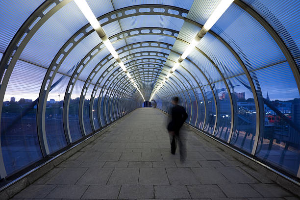 Businessman Walking Through Glass Skywalk at Twilight business commuter on urban elevated walkway at dusk, London, UK, vanishing point stock pictures, royalty-free photos & images