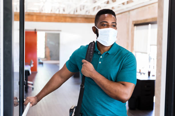 Businessman wearing protective mask leaving work A mid adult businessman leaves his office wearing a protective face mask at the end of the work day. arrival stock pictures, royalty-free photos & images