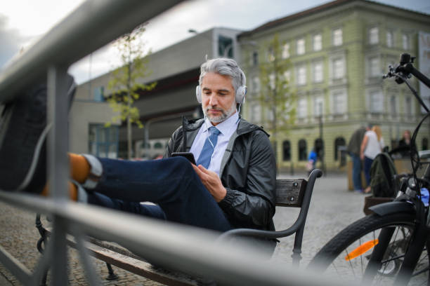 Businessman with bike sitting on bench, listening to music with feet up and resting. Commuting and alternative transport concept stock photo