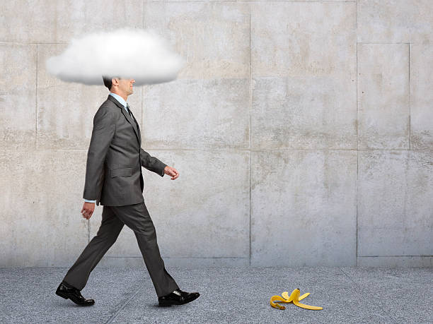 Businessman With Head In Clouds With Banana Peel In Path A banana peel in the path of a businessman walking on a sidewalk with his head in a cloud. ignorance stock pictures, royalty-free photos & images