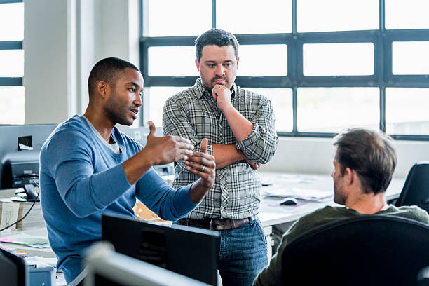 Businessmen discussing in creative office A photo of businessman sharing ideas with colleagues at workplace. Confident male professional is discussing with coworkers. They are wearing smart casuals in creative office. business casual stock pictures, royalty-free photos & images