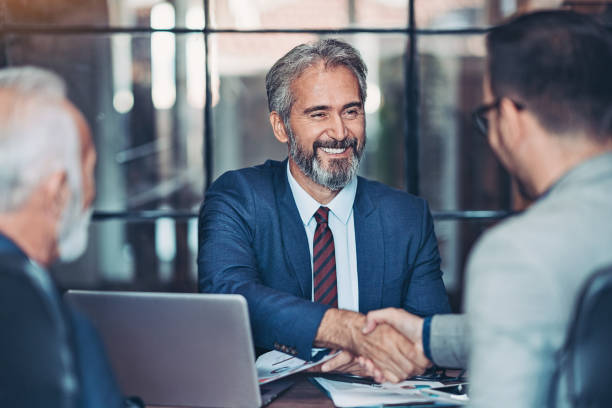 Businessmen handshake in the office Mature businessman shake hands with a younger colleague business stock pictures, royalty-free photos & images