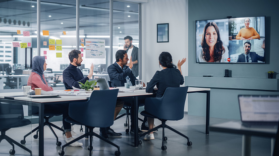 Businesspeople do Video Conference Call with Big Wall TV in Office Meeting Room. Diverse Team of Creative Entrepreneurs at Big Table have Discussion. Specialists work in Digital e-Commerce Startup