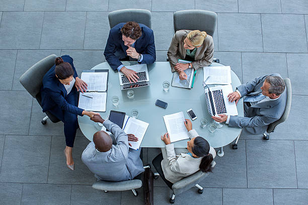 Businesspeople shaking hands at conference table High angle view of businesspeople shaking hands at conference table in office conference table stock pictures, royalty-free photos & images