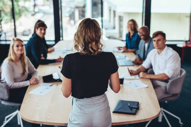Businesswoman addressing a meeting in office Rear view of a businesswoman addressing a meeting in office. Female manager having a meeting with her team in office boardroom. board room stock pictures, royalty-free photos & images