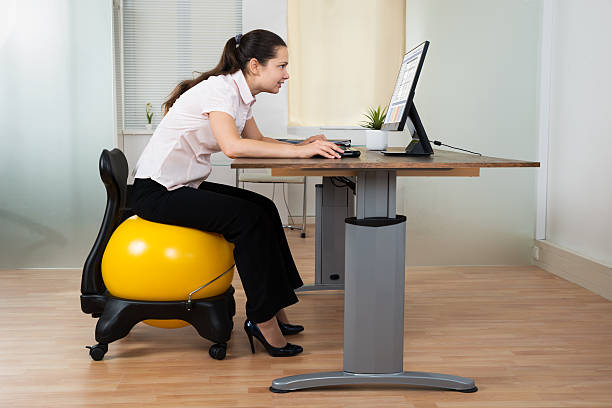 Businesswoman Bending While Sitting On Fitness Ball Businesswoman Bending In Front Of Computer While Sitting On Fitness Ball In Office yoga ball work stock pictures, royalty-free photos & images