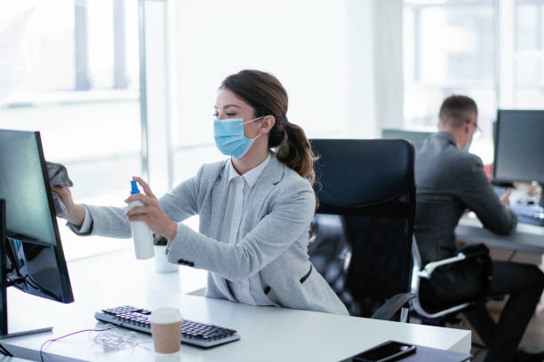 Businesswoman disinfecting monitor in office. Businesswoman disinfecting monitor in office. Covid-19 clean desk stock pictures, royalty-free photos & images