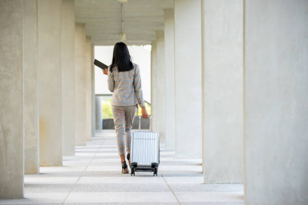 Businesswoman Dragging suitcase luggage bag, walking to passenger boarding in Airport. Working woman travel to work. Asian tourist female wearing suit pull trolley bag. Businesswoman Travel concept stock photo