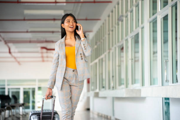 Businesswoman Dragging suitcase luggage bag, walking to passenger boarding in Airport. Woman travel to work. Asian tourist female wearing suits and using smartphone. Businesswoman Travel concept stock photo