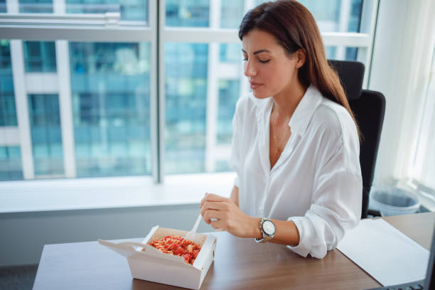 Businesswoman eating take out lunch from the box at her desk stock photo