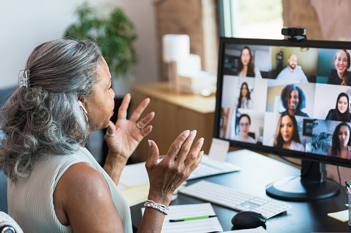 A serious senior businesswoman gestures as she facilitates a staff meeting while working from home. She is talking with her colleagues during a video conference.