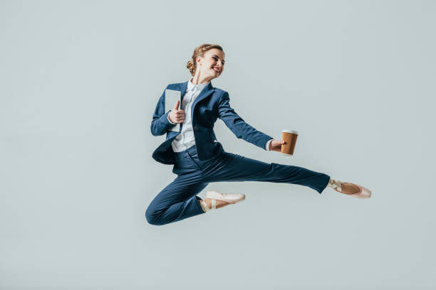 businesswoman in suit and ballet shoes jumping with coffee and digital tablet businesswoman in suit and ballet shoes jumping with coffee and digital tablet, isolated on grey flexibility stock pictures, royalty-free photos & images
