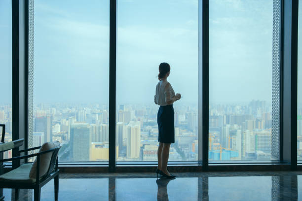 Businesswoman looking at city skyline through office window stock photo