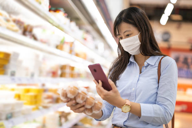businesswoman picks up eggs asian young businesswoman wear face mask who is shopping for fresh eggs and scanning barcode with smart phone at supermarket medical scan stock pictures, royalty-free photos & images