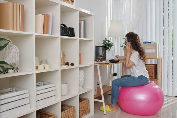 Businesswoman Sitting on Fitness Ball Young businesswoman sitting on fitness ball when working at her home office and attending online conference with colleagues yoga ball work stock pictures, royalty-free photos & images