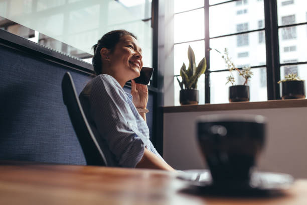 Businesswoman talking on mobile phone in office Smiling young female business professional making a phone call. Asian businesswoman talking on mobile phone in office. small business saturday stock pictures, royalty-free photos & images
