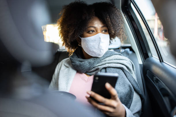 Businesswoman traveling by taxi during COVID-19 pandemic Mixed race woman with protective face mask travel by taxi. Businesswoman traveling by taxi during COVID-19 pandemic. riding stock pictures, royalty-free photos & images