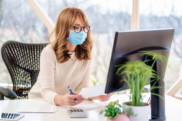 Businesswoman wearing face mask while working at the office stock photo