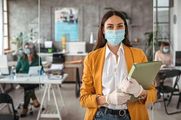 Businesswoman with protective gloves and face mask at office Portrait of businesswoman with protective gloves and face mask after returning back to work at office returning stock pictures, royalty-free photos & images