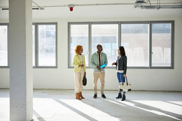 Businesswomen in 20s and 30s Discussing Property with Broker Full length front view of diverse group in 20s and 30s standing in shell condition office space discussing potential use. property management companies stock pictures, royalty-free photos & images
