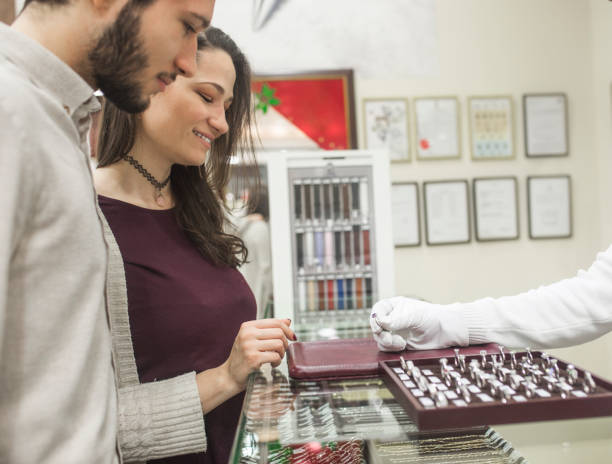 Buying a  engagement ring Young couple baying a engagement ring in jewelry store store clerk selling jewelry stock pictures, royalty-free photos & images