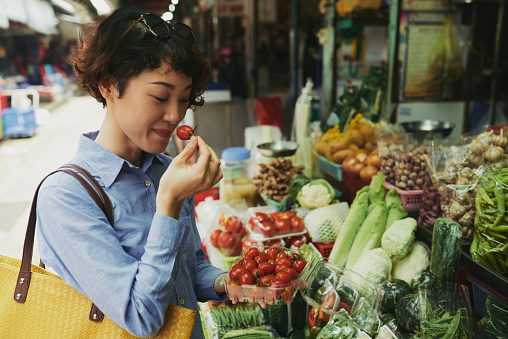 Japanese woman smelling cherry tomatoes at market counter