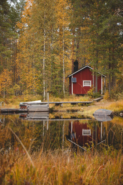 Cabin with boat dock in autumn colours in tiilikkajarvi national park, kainuu, Finland. Red cottage combination with orange leaves of deciduous trees stock photo