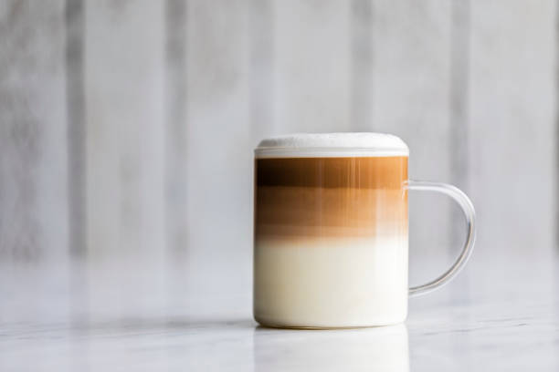Cafe latte macchiato layered coffee Cafe latte macchiato layered coffee in a see through glass coffee cup. The cup has a white wooden background. frothy drink stock pictures, royalty-free photos & images