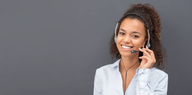Call center employee isolated on a gray background. Call center worker isolated on a gray background. Smiling customer support operator at work. Young employee working with a headset. headset woman customer service stock pictures, royalty-free photos & images