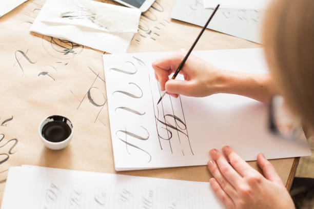 calligraphy, handwriting, technique concept. woman with beautiful elegant hands inscribing capital russian letters carefully in italic type with black ink and thin brush, drawing stock photo