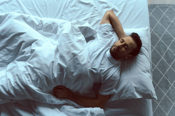 Calm handsome man sleeping on white linen Top view of serene attractive male lying in comfortable bed and happily dreaming stock photo man sleeping in bed top view stock pictures, royalty-free photos & images
