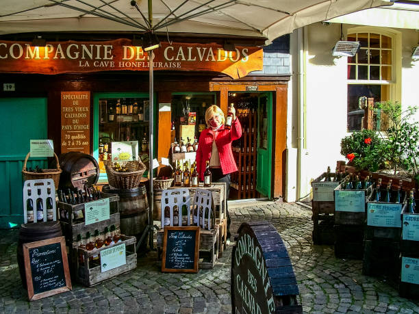 Calvados shop in  Honfleur, France Honfleur, France - October 20, 2005: Shop-bar selling Calvados - one of the gastronomic symbols of Normandy. A woman holds in her hand one of the bottles of this drink. calvados stock pictures, royalty-free photos & images