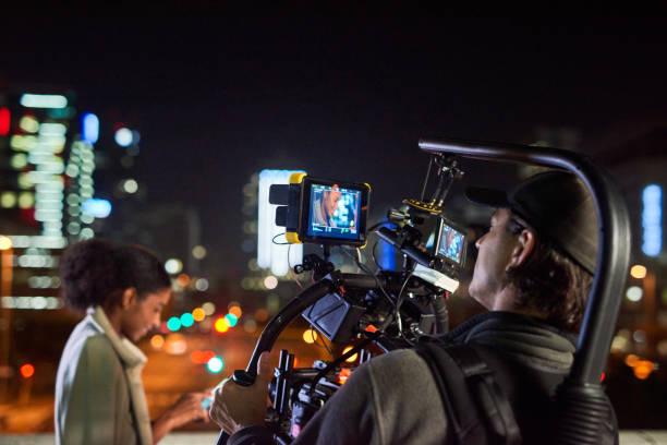 Camera, lights, action! Behind the scenes shot of a camera operator shooting a scene with a businesswoman at night camera operator stock pictures, royalty-free photos & images