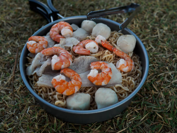 Camping food Instant noodles or mama stir in a small camping pan. Decorate the dish with prawns, pork sliders and meatballs. Suitable for morning atmosphere stock photo