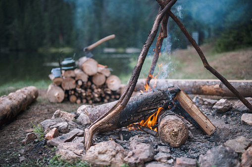 Photo of a campfire in a campsite with wood material and a vintage ax and teapot